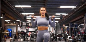 female doing a reverse lung with a barbell in a gym