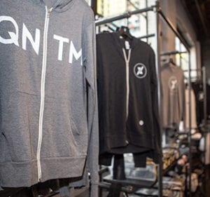 an assortment of zip up hoodies and shirts hanging on merchandise racks in the pro shop at qntm fit life