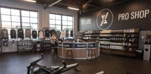 wide angle image of the pro shop at qntm fit life with clothing racks and workout supplement racks and pro shop decal on wall surrounding the personal training desk