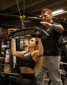 female using lat pull down machine at qntm fit life with personal trainer standing close by coaching her